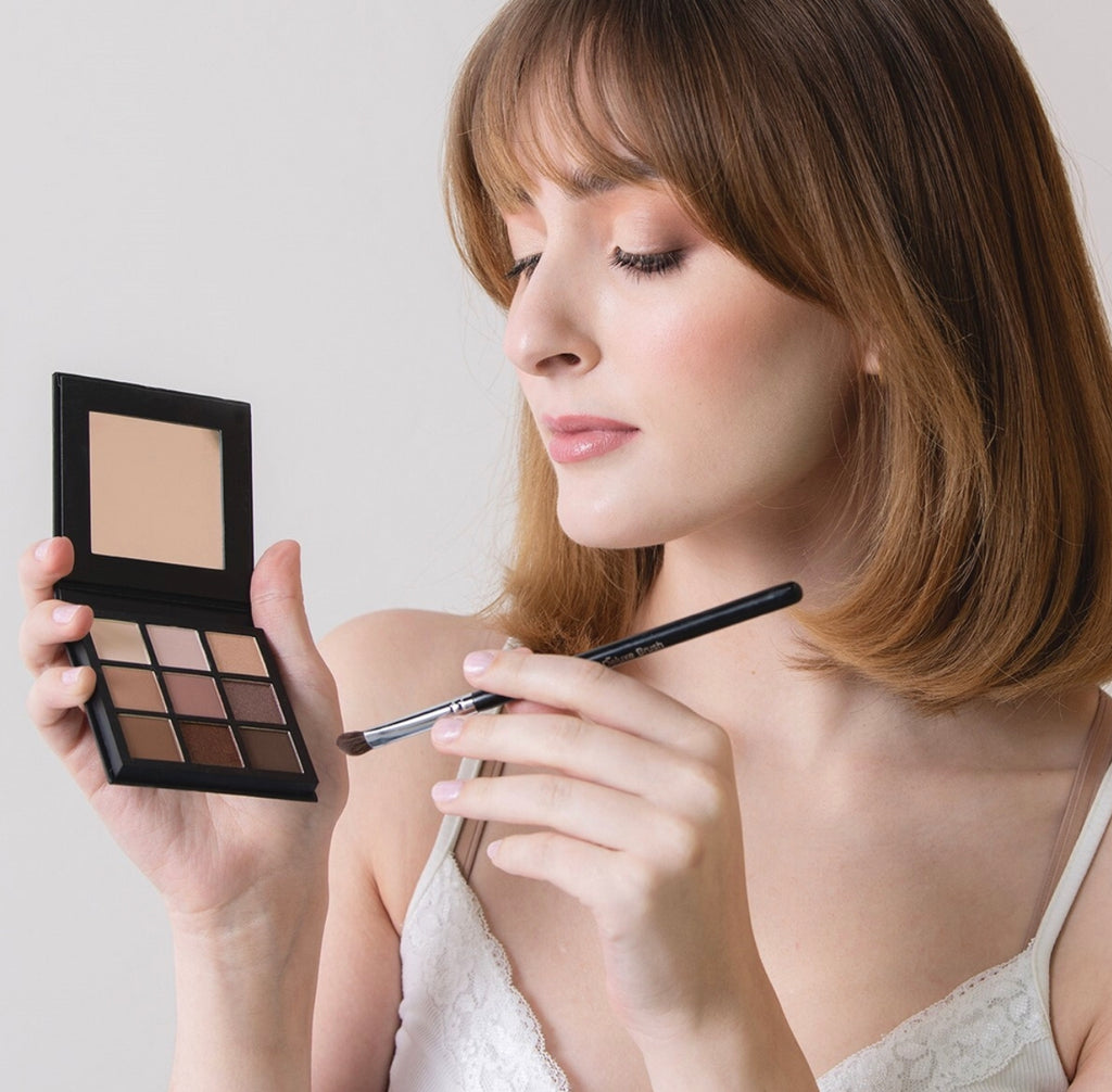 Beautiful short brown haired woman applying a Shine Cosmetics neutral shade eyeshadow palette with a makeup brush